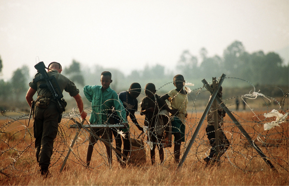 A French soldier, one of the international forces supporting the relief effort adjusts the concertina wire surrounding the airport while Rwandan refugee children watch